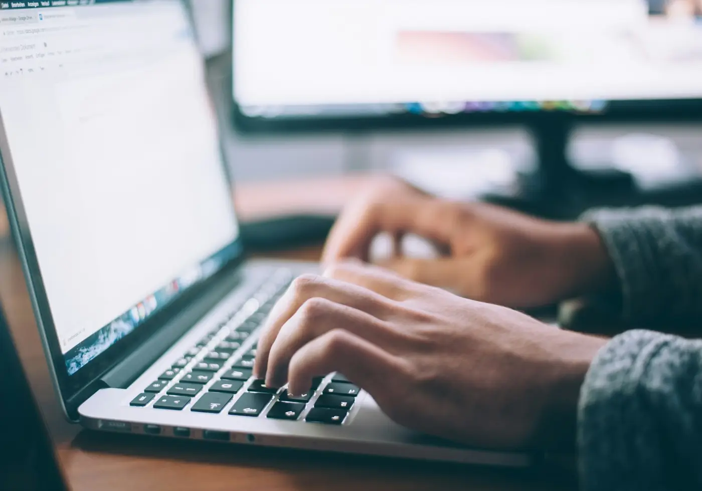 Hands typing on a laptop at a desk
